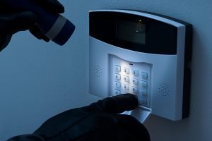 Picture of someone looking at the keypad of a burglar alarm with a torch, wearing black gloves